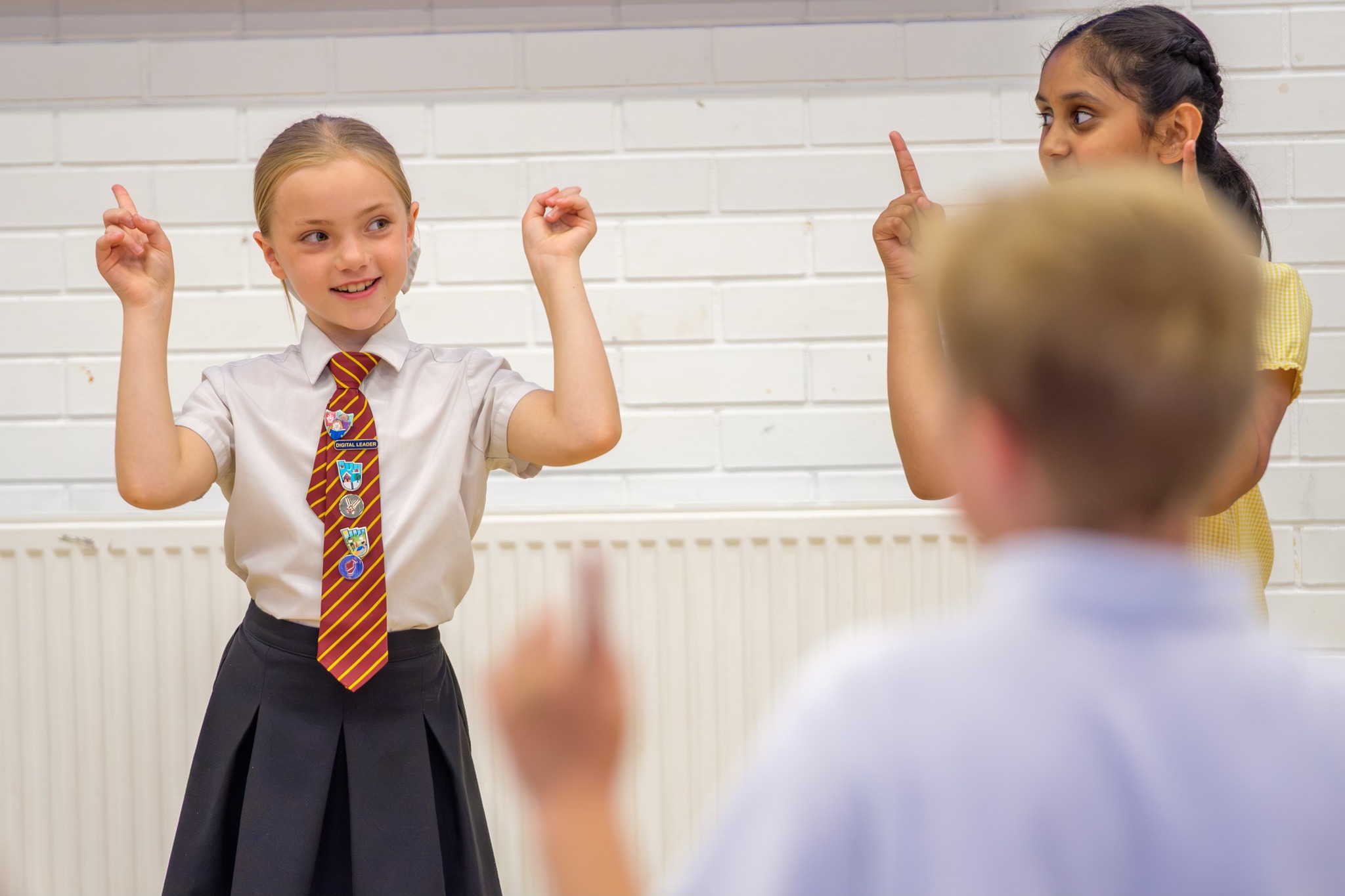 Two girls in school uniform are performing actions to a song. They're pointing their fingers up in the air.
